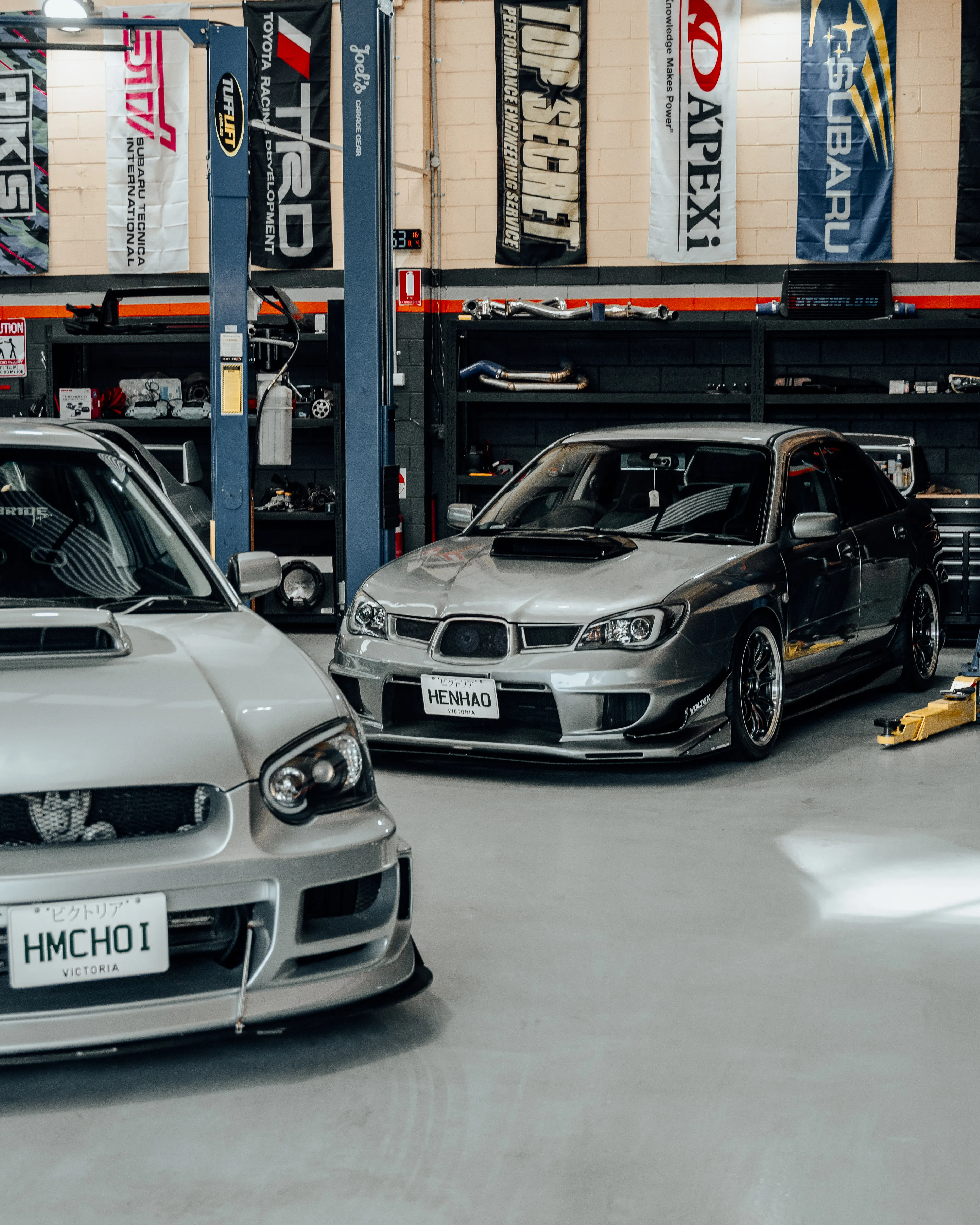 Two Subarus in the Wangan Performance workshop with HKS and TRD banners
