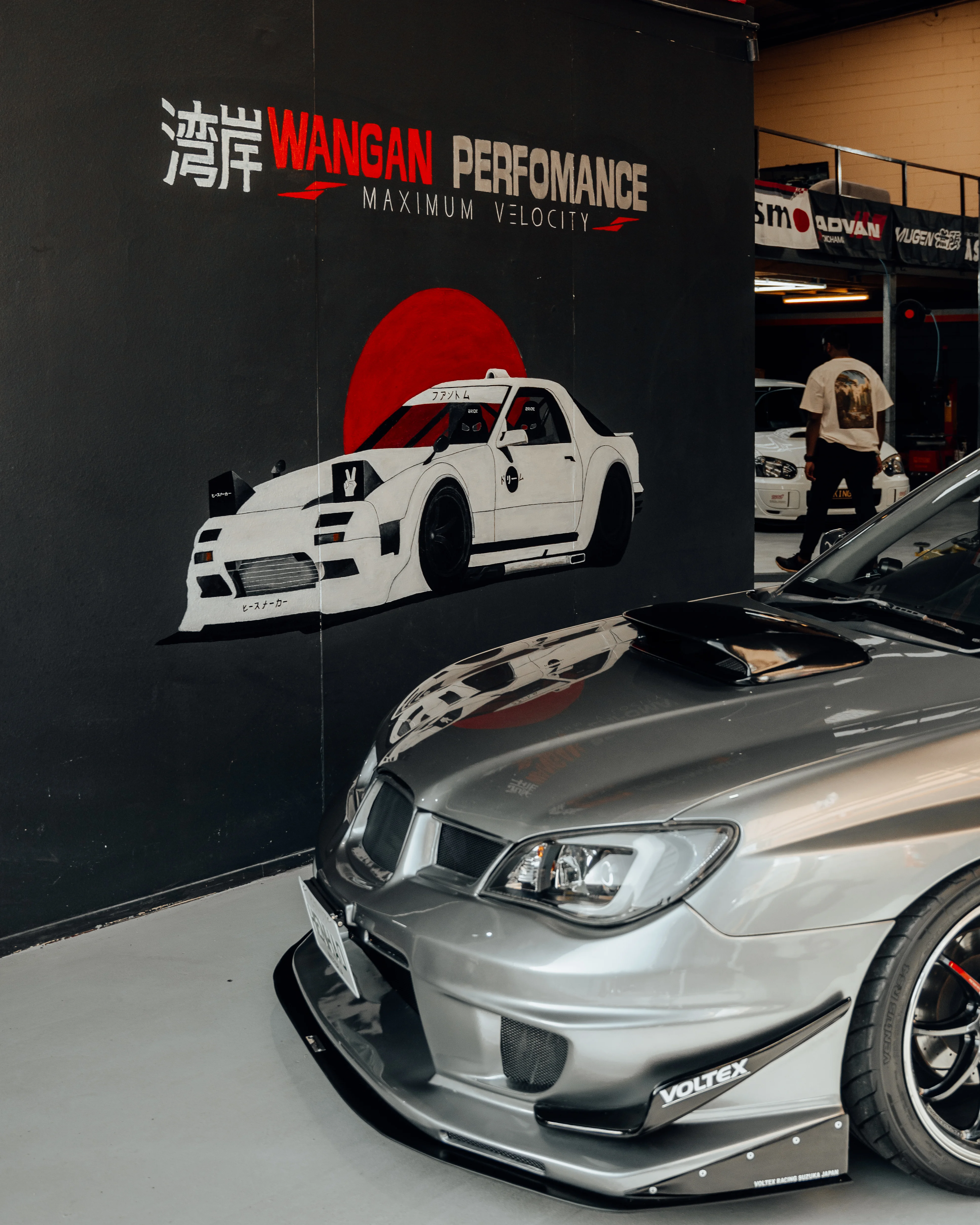 Wangan Performance mural wall beside a silver Subaru WRX