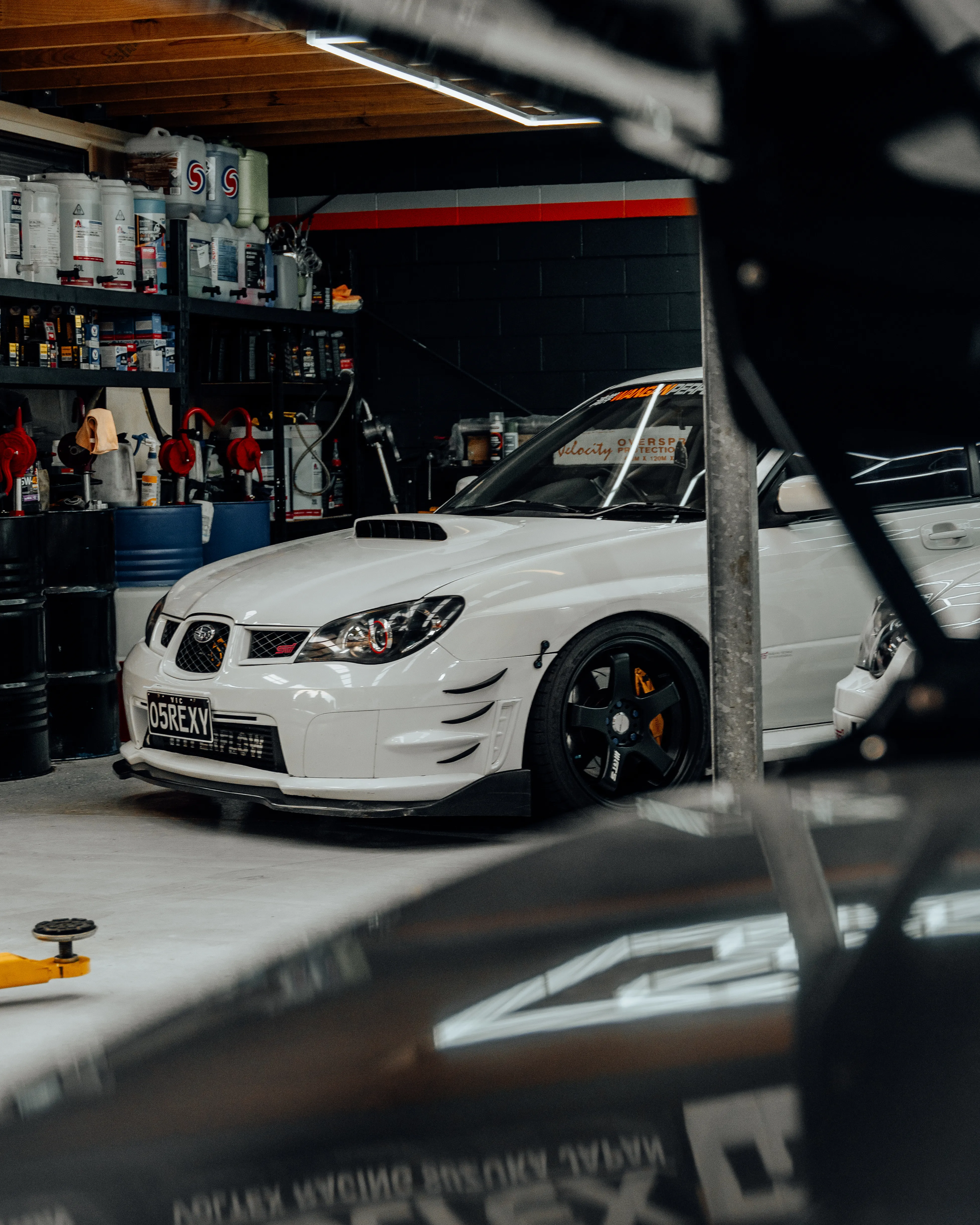 White Subaru STI seen through workshop hoist frame at Wangan Performance